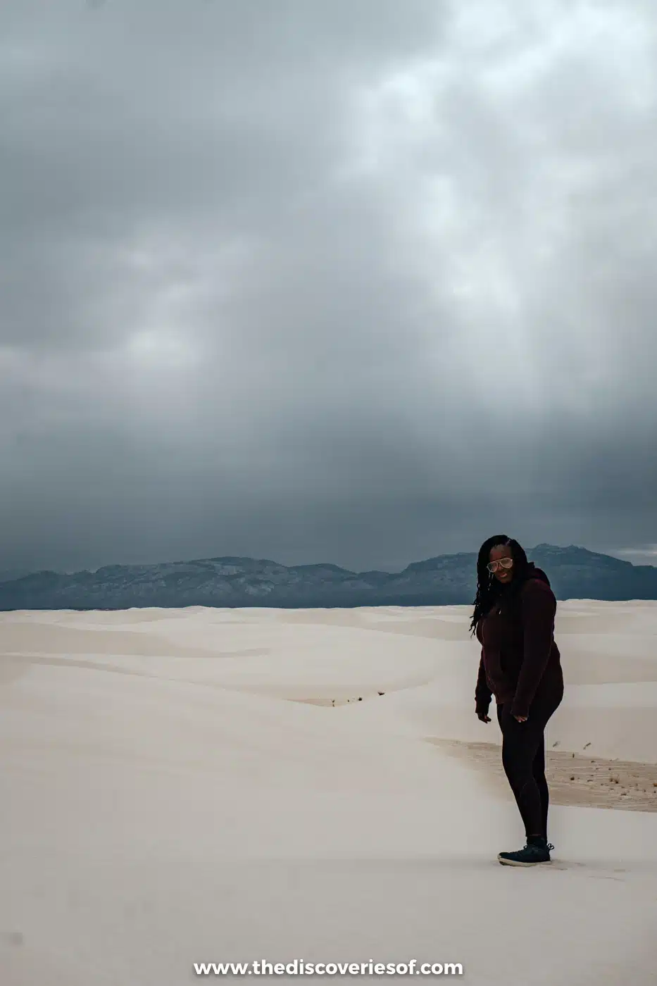 Julianna standing on the white gypsum dunes of White Sands National Park under heavy grey rain clouds in February