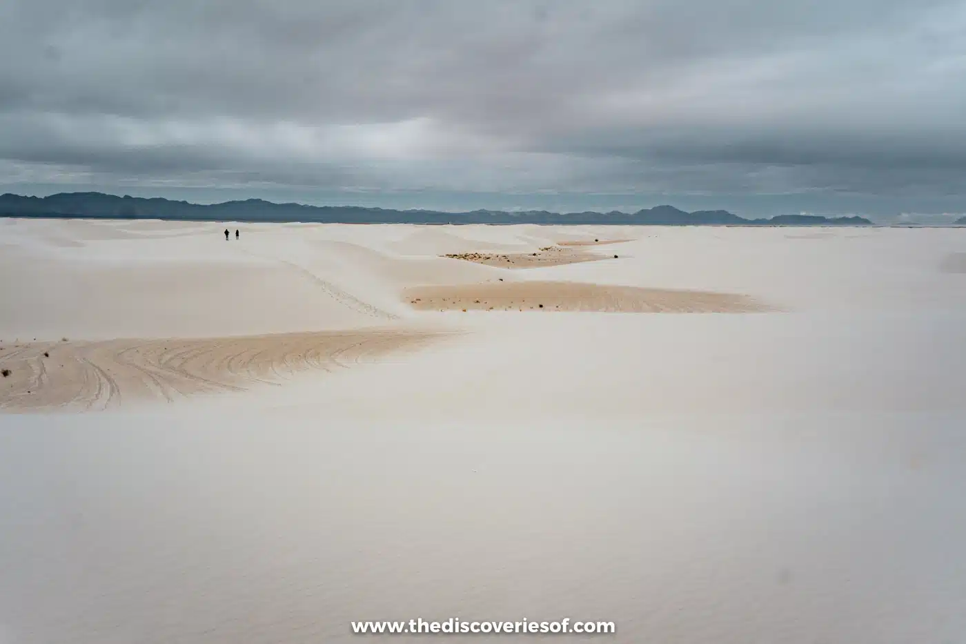 Two distant walkers crossing a wide white gypsum dunefield towards the mountains at White Sands National Park