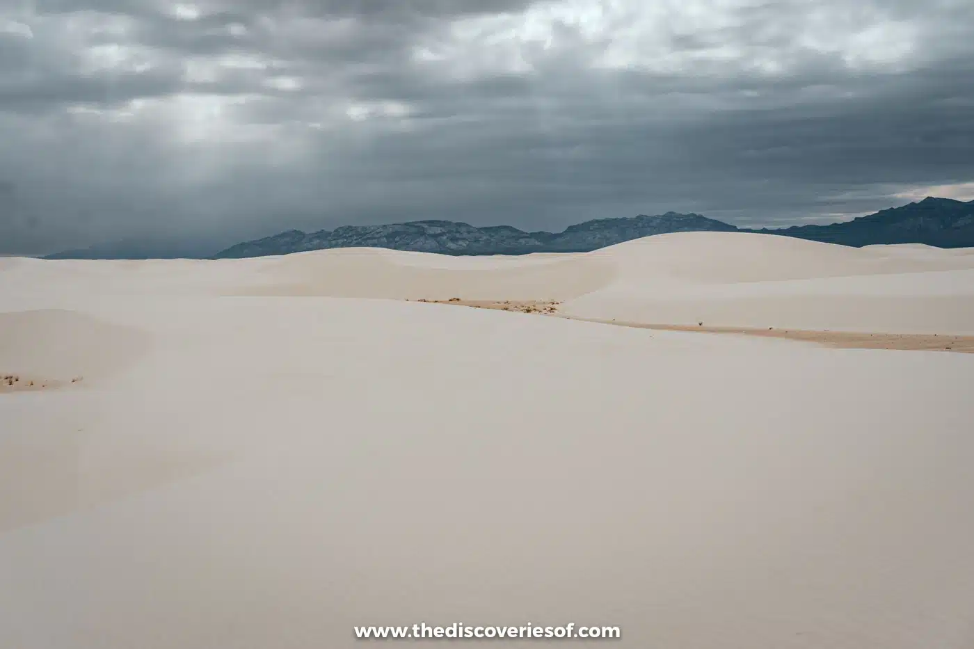 Rolling white gypsum dunes stretching to a dark mountain range under stormy grey cloud at White Sands National Park