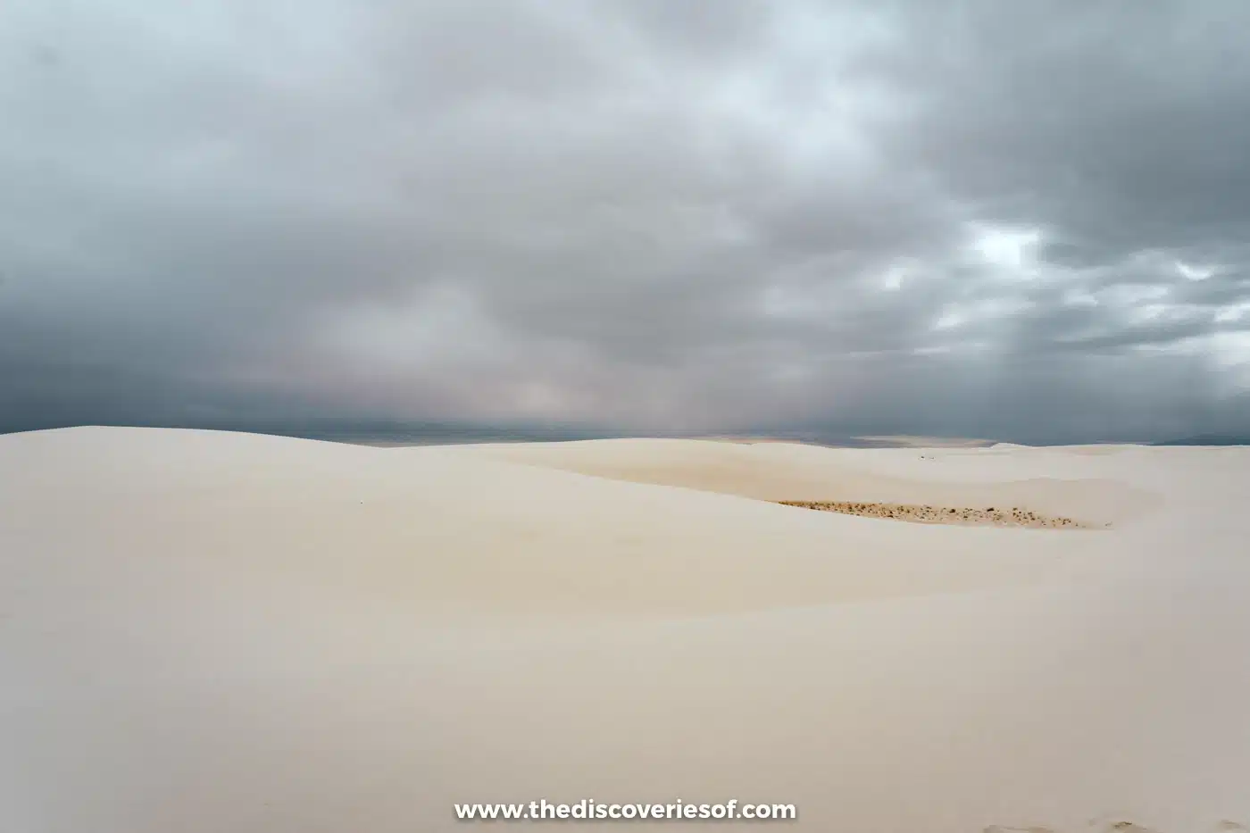Smooth white gypsum dunes stretching beneath heavy grey storm clouds at White Sands National Park