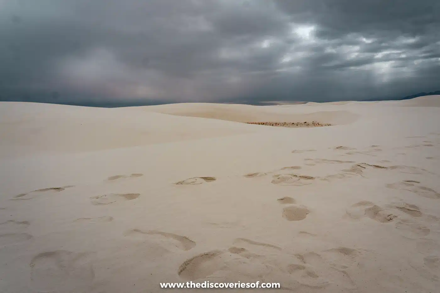 Footprints across soft white gypsum sand beneath a heavy grey sky at White Sands National Park