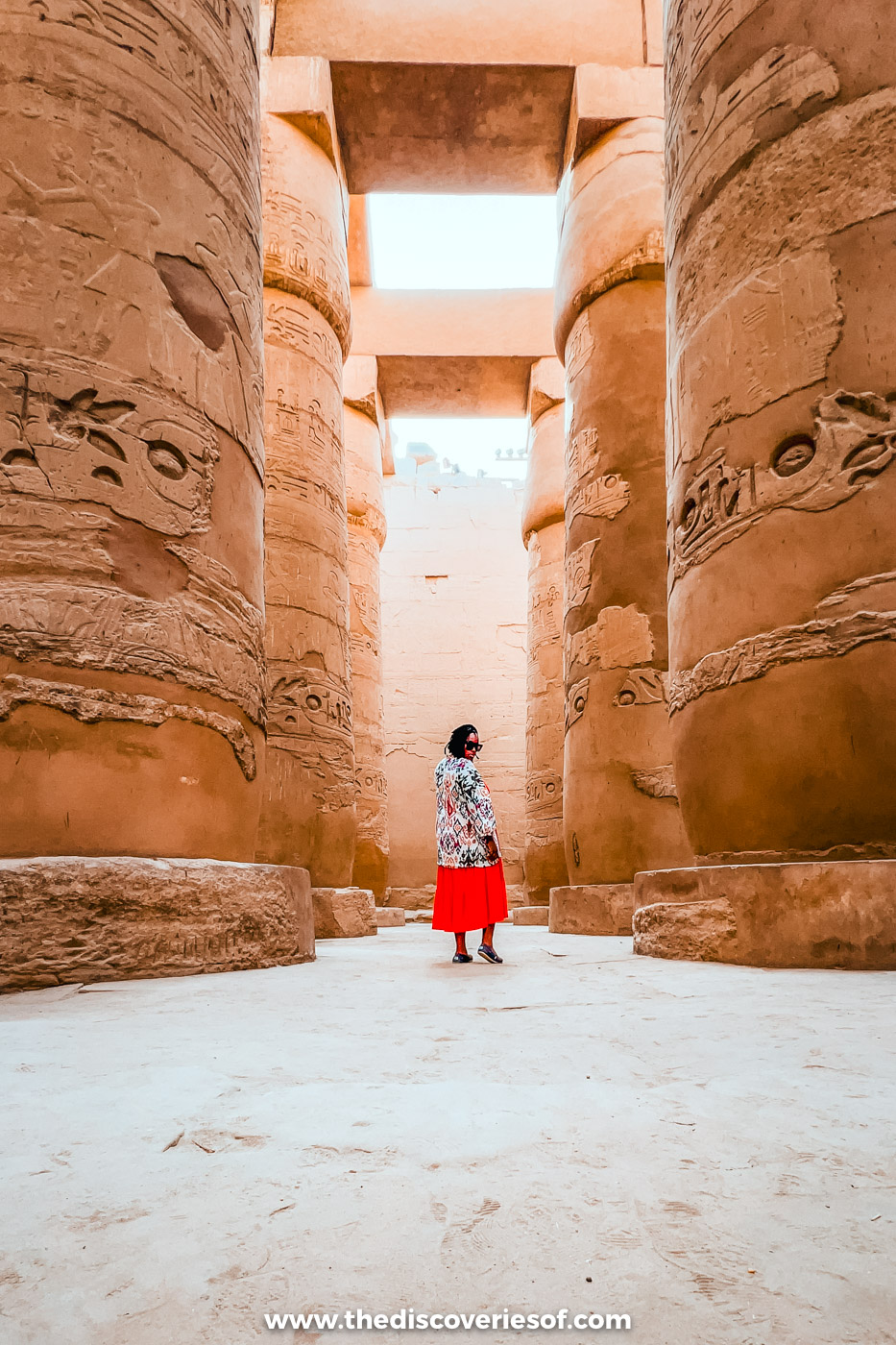 Julianna in a red maxi skirt and light kimono looking up among the giant columns of Karnak's Great Hypostyle Hall